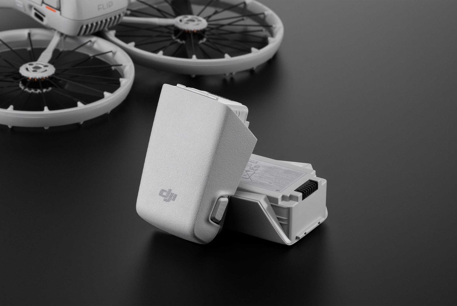 A DJI Flip drone placed on a dark reflective surface, accompanied by two intelligent flight batteries, one standing upright and the other lying flat, showcasing their compact design and branding.